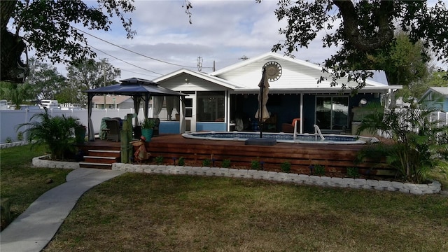 rear view of house featuring a deck, a gazebo, a sunroom, and a lawn