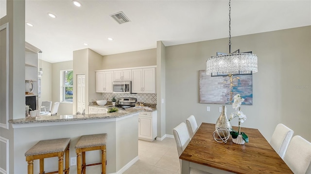 kitchen featuring kitchen peninsula, pendant lighting, stainless steel appliances, light stone countertops, and white cabinets