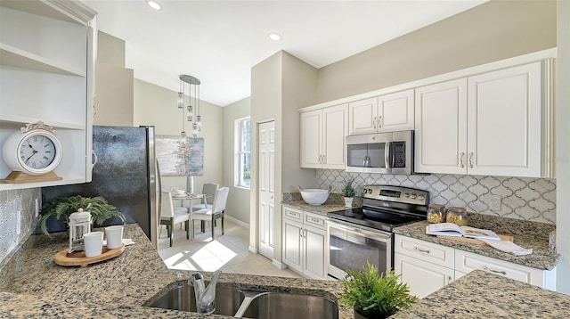 kitchen with sink, stone counters, white cabinetry, hanging light fixtures, and stainless steel appliances