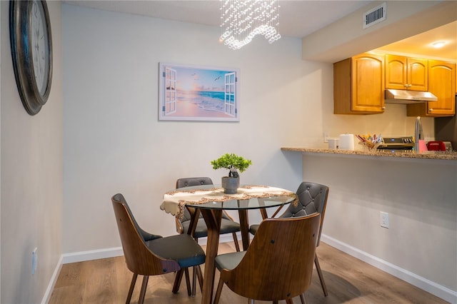 dining area featuring light wood-type flooring, sink, and a notable chandelier