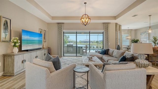 living room featuring a tray ceiling, an inviting chandelier, and light hardwood / wood-style flooring