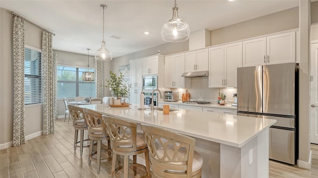 kitchen featuring pendant lighting, white cabinetry, stainless steel appliances, a kitchen island with sink, and a breakfast bar