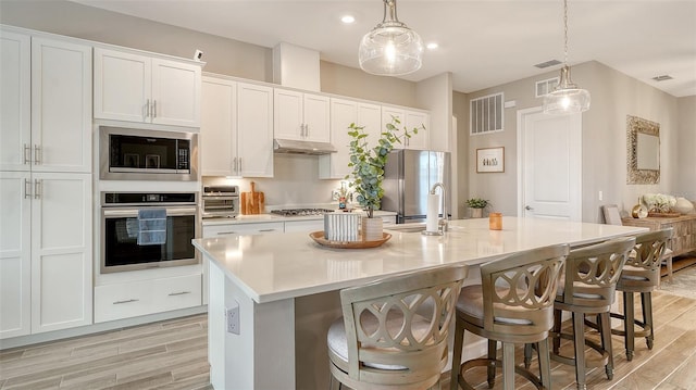 kitchen with white cabinets, appliances with stainless steel finishes, and an island with sink