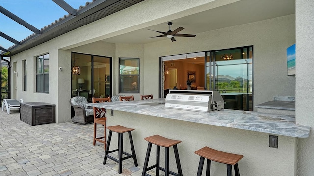 view of patio with ceiling fan, a bar, exterior kitchen, and grilling area