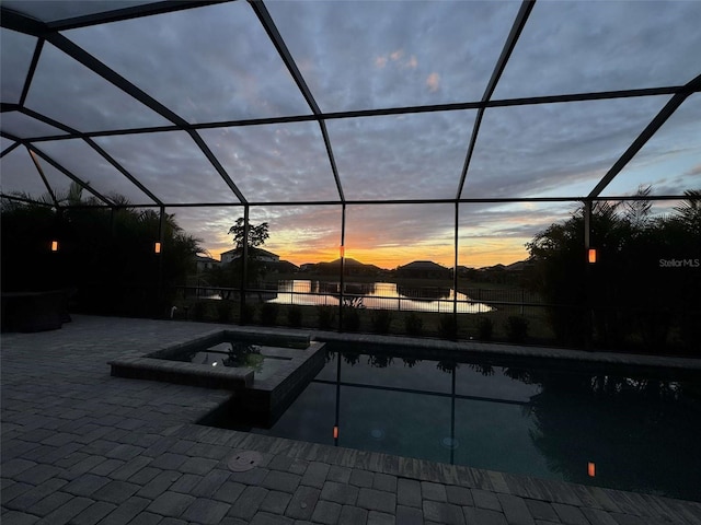 pool at dusk with glass enclosure, a patio area, and an in ground hot tub