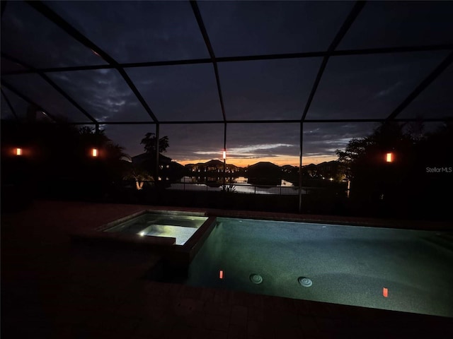 pool at dusk with a lanai and an in ground hot tub