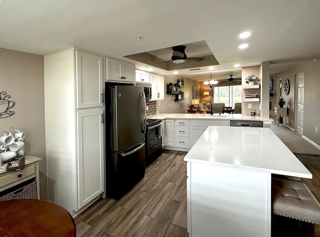 kitchen with black appliances, kitchen peninsula, white cabinetry, and a raised ceiling