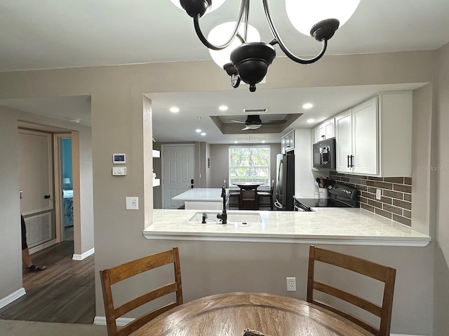 kitchen with white cabinetry, kitchen peninsula, backsplash, black appliances, and sink