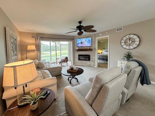 living room featuring ceiling fan, carpet, and a stone fireplace