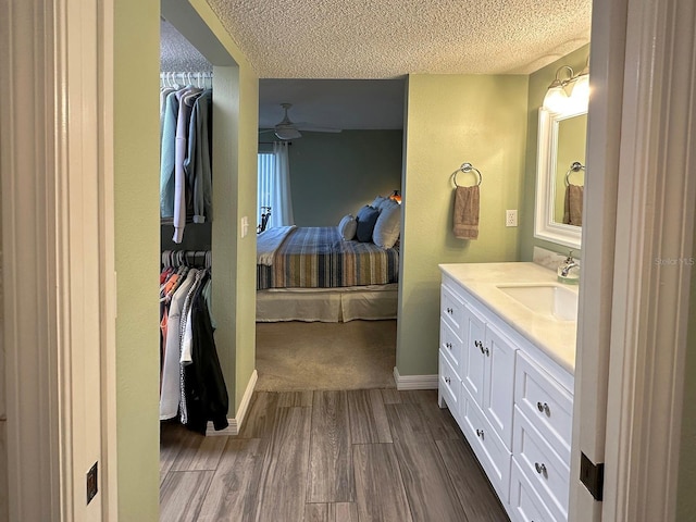 bathroom with a textured ceiling, ceiling fan, wood-type flooring, and vanity