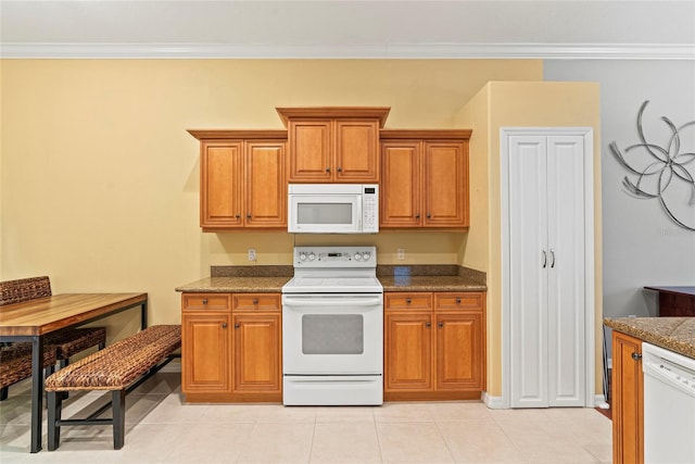 kitchen featuring dark stone counters, light tile patterned flooring, white appliances, and ornamental molding