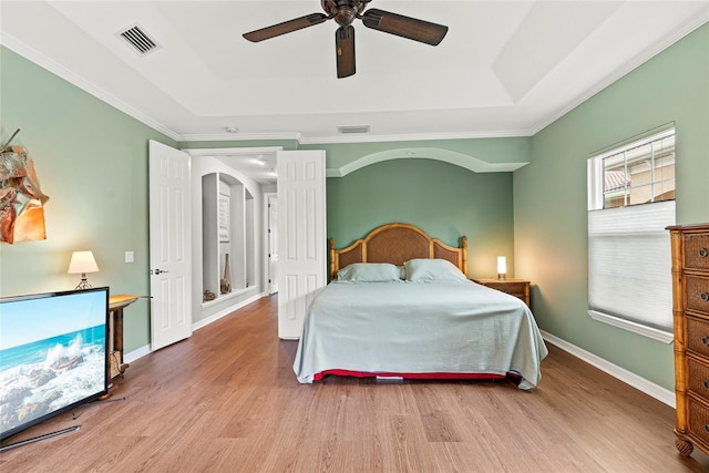 bedroom with ceiling fan, hardwood / wood-style floors, crown molding, and a raised ceiling