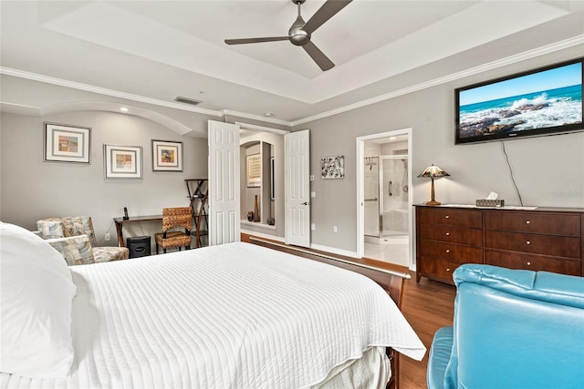 bedroom featuring hardwood / wood-style floors, ensuite bathroom, ornamental molding, ceiling fan, and a tray ceiling