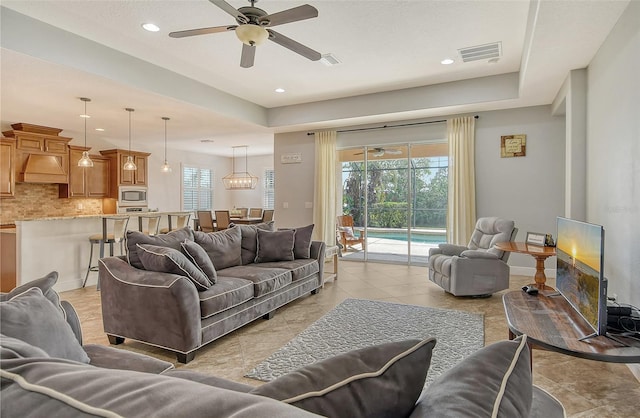 living room with a tray ceiling, ceiling fan, and light tile patterned flooring