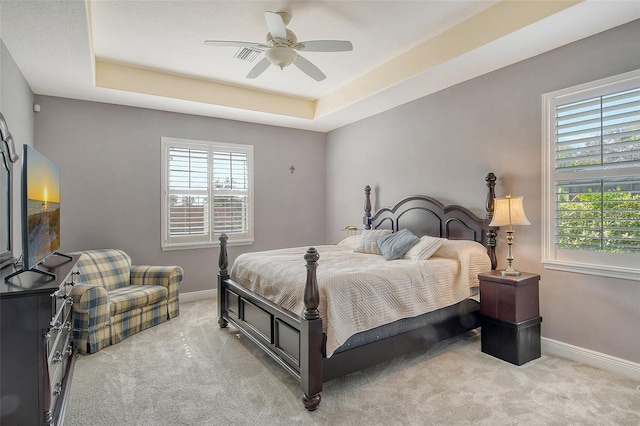 bedroom with multiple windows, light colored carpet, and a raised ceiling