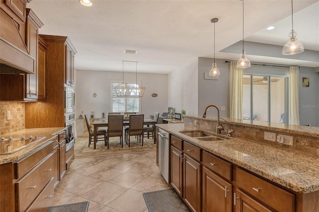 kitchen featuring sink, stainless steel appliances, tasteful backsplash, custom range hood, and decorative light fixtures