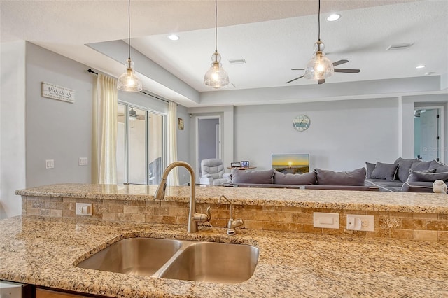 kitchen with sink, hanging light fixtures, ceiling fan, light stone counters, and a textured ceiling