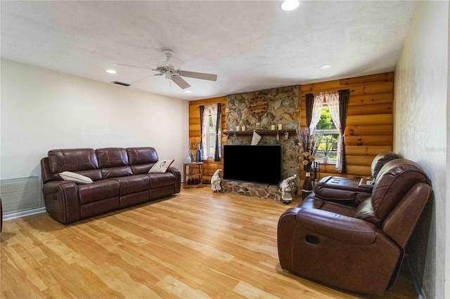 living room featuring a textured ceiling, log walls, a stone fireplace, light wood-type flooring, and ceiling fan