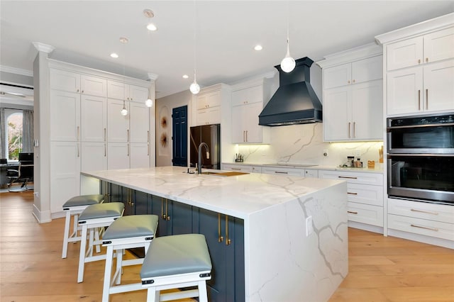 kitchen with stainless steel double oven, custom exhaust hood, decorative light fixtures, white cabinetry, and a large island