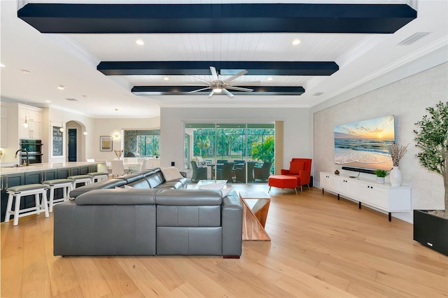 living room featuring ceiling fan, light wood-type flooring, beamed ceiling, and crown molding