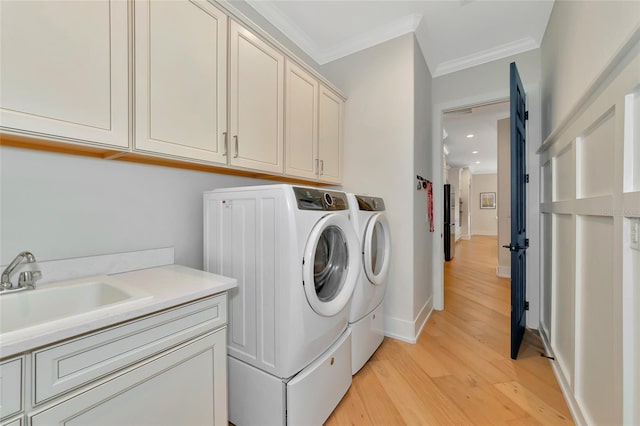 laundry area with sink, light hardwood / wood-style flooring, separate washer and dryer, ornamental molding, and cabinets