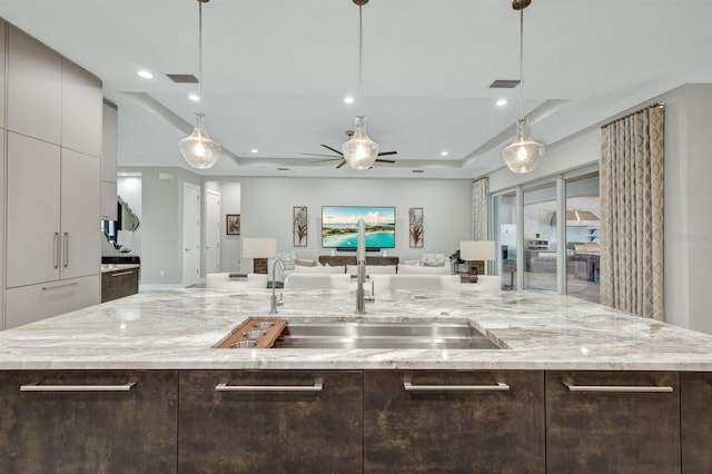 kitchen with sink, a kitchen island with sink, dark brown cabinets, and light stone countertops