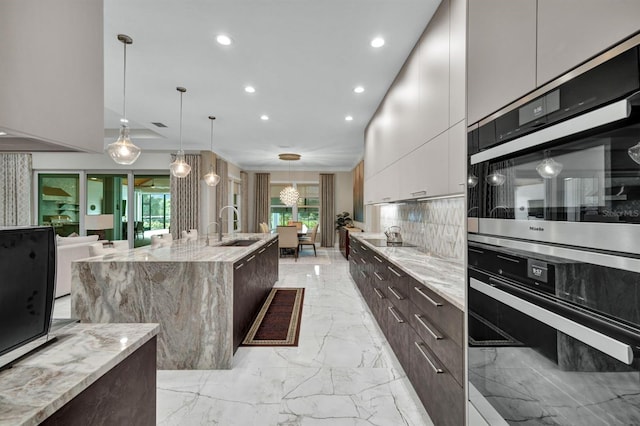 kitchen with decorative light fixtures, tasteful backsplash, a center island with sink, sink, and white cabinetry