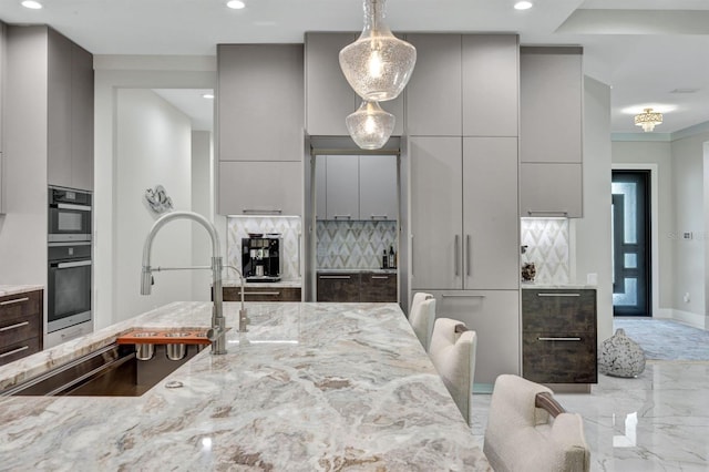 kitchen featuring light stone countertops, decorative light fixtures, tasteful backsplash, sink, and gray cabinets