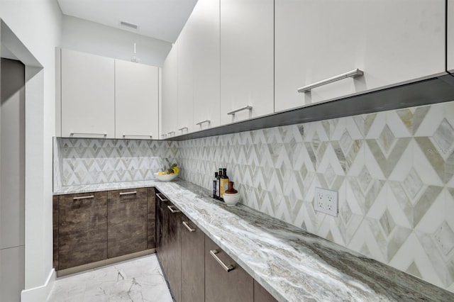 kitchen featuring white cabinets, backsplash, light stone countertops, and dark brown cabinets