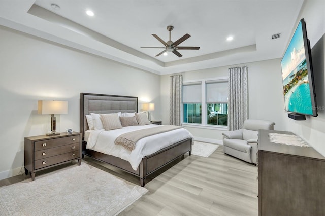 bedroom with ceiling fan, a tray ceiling, and light hardwood / wood-style flooring