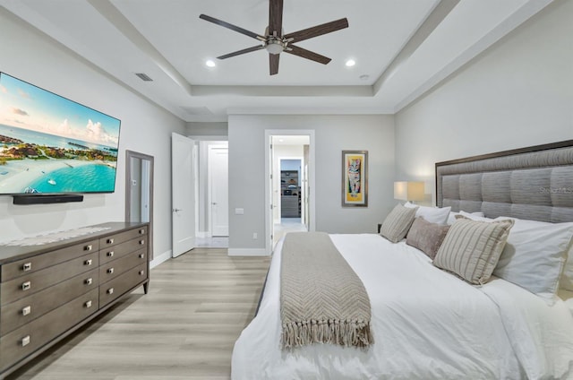 bedroom featuring light wood-type flooring, ceiling fan, and a tray ceiling