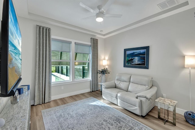 living room featuring light hardwood / wood-style floors, a raised ceiling, and ceiling fan