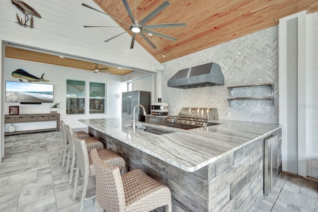 kitchen with wood ceiling, high quality fridge, lofted ceiling, wall chimney exhaust hood, and a breakfast bar