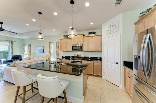 kitchen featuring pendant lighting, appliances with stainless steel finishes, sink, dark stone countertops, and a center island with sink