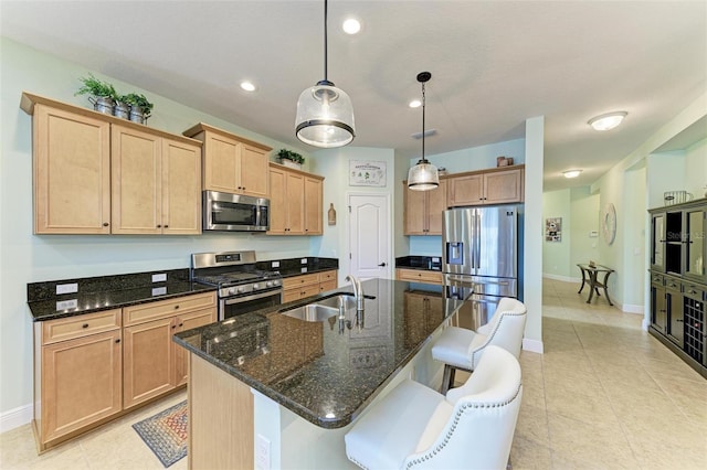 kitchen with decorative light fixtures, sink, a kitchen island with sink, dark stone countertops, and stainless steel appliances