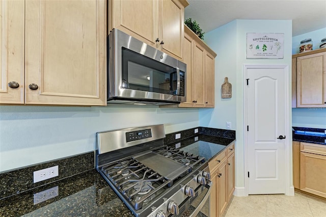 kitchen featuring light tile patterned floors, light brown cabinets, appliances with stainless steel finishes, and dark stone counters