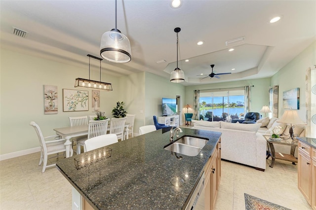 kitchen featuring sink, an island with sink, a raised ceiling, and pendant lighting