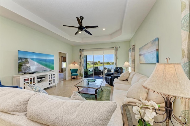 tiled living room with ceiling fan and a raised ceiling