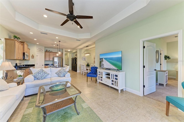 living room with ceiling fan, a raised ceiling, and light tile patterned flooring