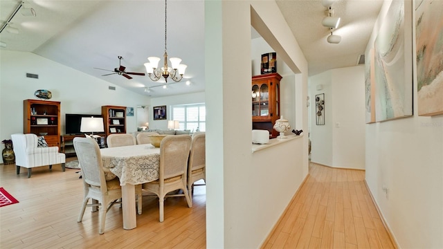 dining space with ceiling fan with notable chandelier, rail lighting, vaulted ceiling, and light wood-type flooring