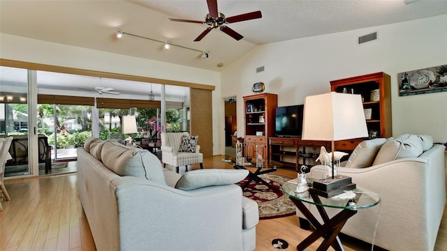 living room with ceiling fan, light wood-type flooring, vaulted ceiling, and a textured ceiling