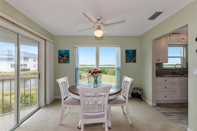 dining space with ceiling fan, sink, light carpet, and a textured ceiling