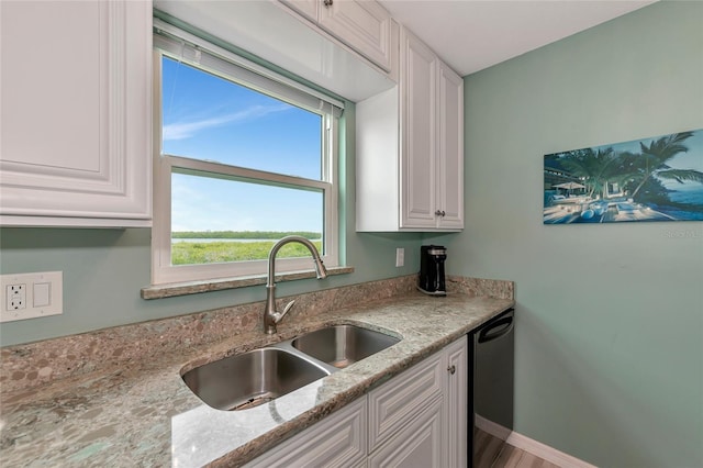 kitchen featuring a wealth of natural light, dishwasher, sink, white cabinets, and light stone countertops