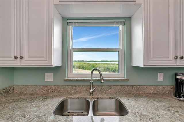 kitchen with white cabinetry, light stone countertops, and sink