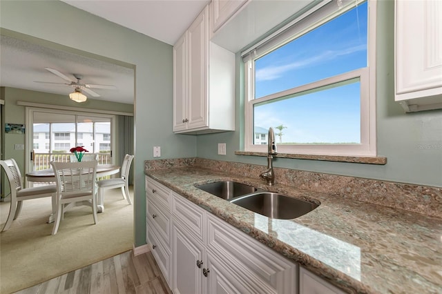 kitchen with a wealth of natural light, sink, white cabinets, light stone countertops, and light wood-type flooring