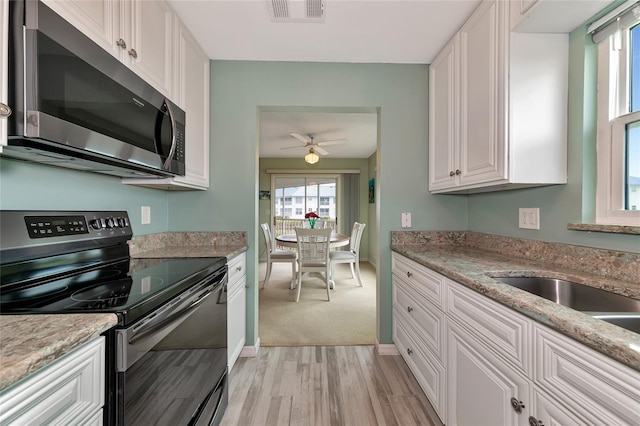 kitchen with white cabinets, ceiling fan, light stone counters, black range with electric stovetop, and light hardwood / wood-style flooring