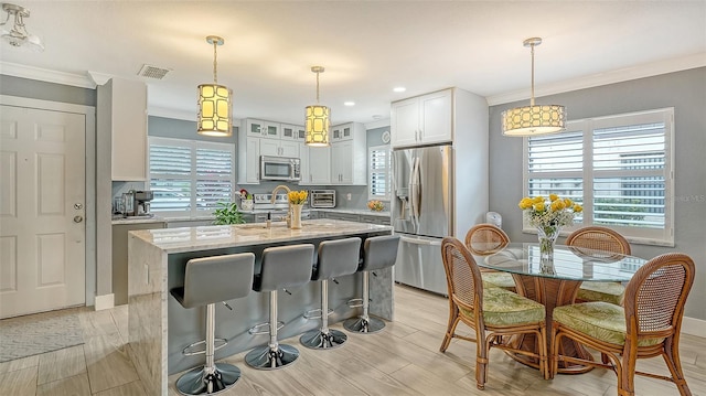 kitchen with light stone countertops, white cabinets, stainless steel appliances, plenty of natural light, and a center island with sink