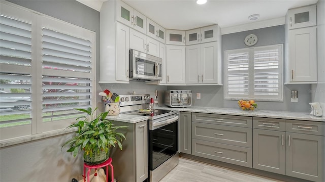 kitchen featuring appliances with stainless steel finishes, white cabinets, ornamental molding, light stone counters, and gray cabinets