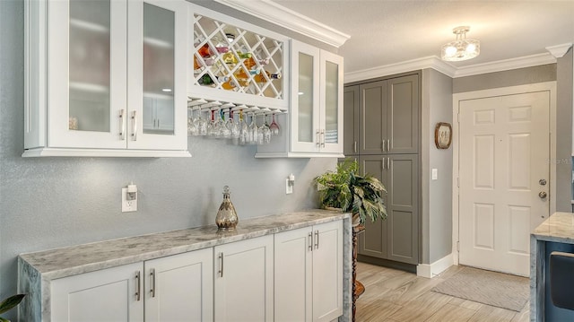 bar featuring white cabinets, light wood-type flooring, light stone countertops, and ornamental molding