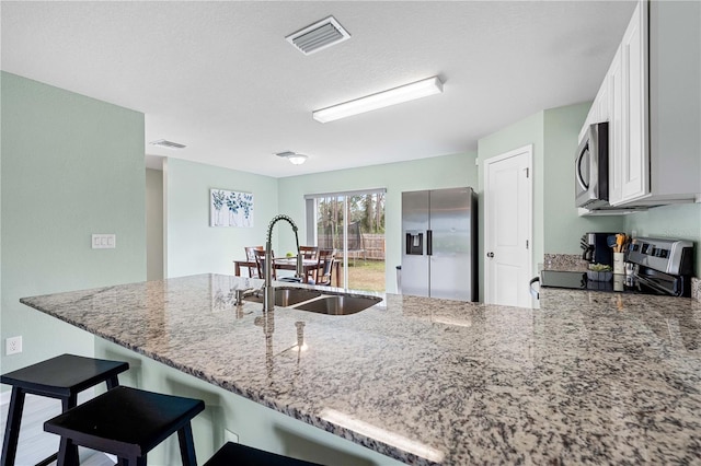 kitchen featuring light stone countertops, white cabinetry, stainless steel appliances, sink, and kitchen peninsula